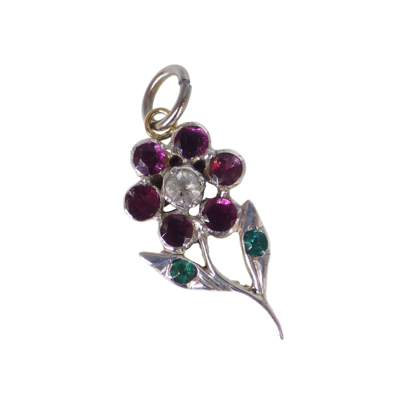 An antique-style floral pendant charm featuring a silver-toned metal setting with a central clear round stone surrounded by six deep pinkish-red round stones, with two green accent stones on leaf-shaped settings below, all on a plain white background.